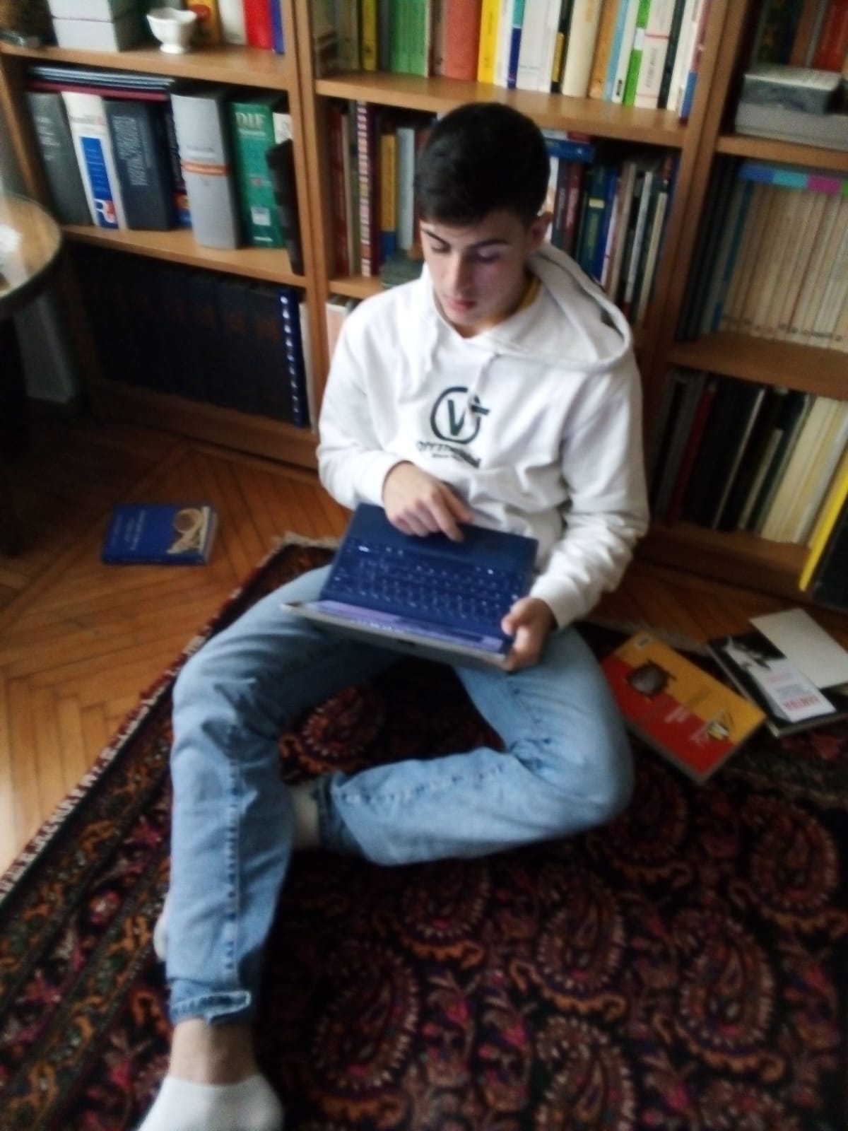 Foto. Jugendlicher sitzt auf dem Boden und arbeitet an einem Notebook.